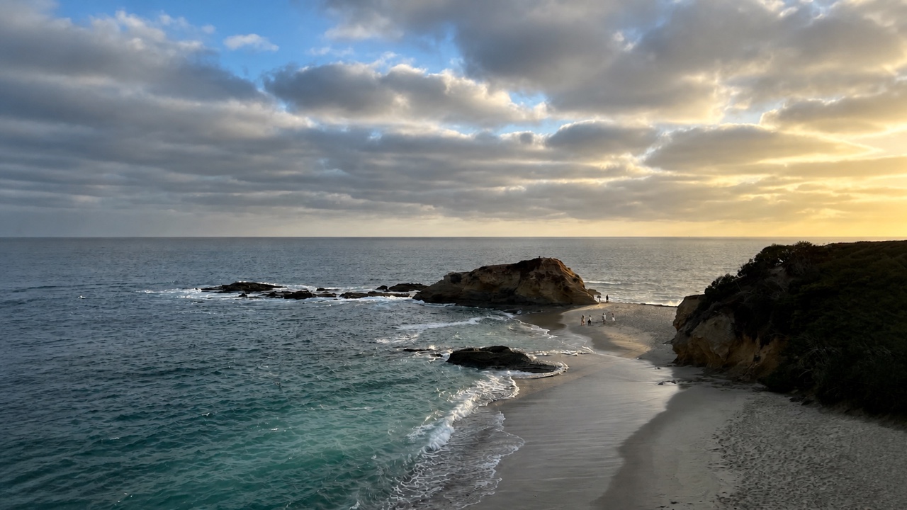 A rocky cove and curving shoreline beneath dramatic clouds at sunset.